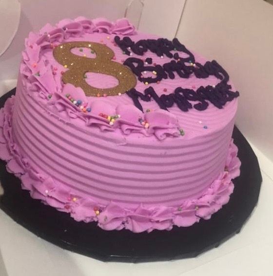 Purple birthday cake with gold number eight topper and piped frosting on edges.