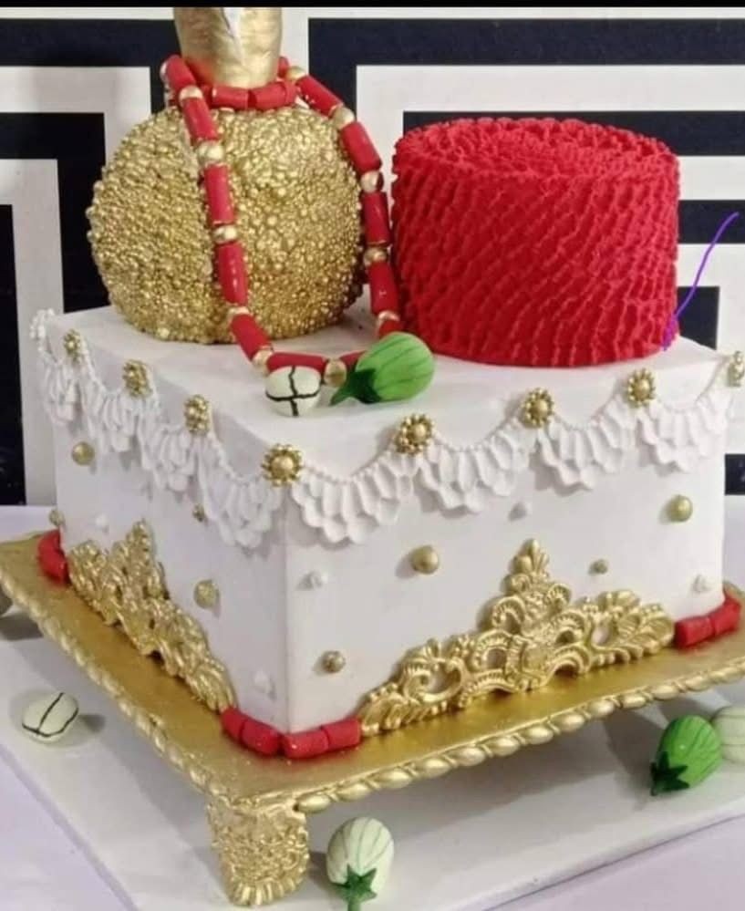 Ornate cake with gold and red decorations, featuring a textured sphere and cylinder on top.