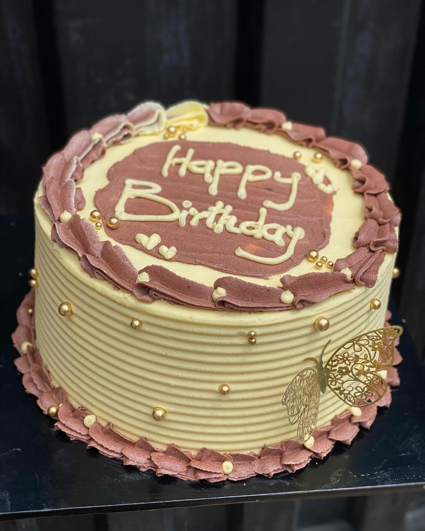 Decorative birthday cake with pink and white frosting, gold beads, and a butterfly embellishment.