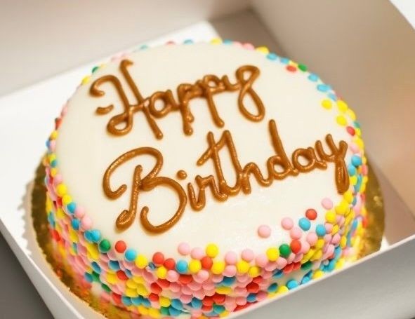 Birthday cake with white icing, colorful sprinkles, and 'Happy Birthday' written on top.
