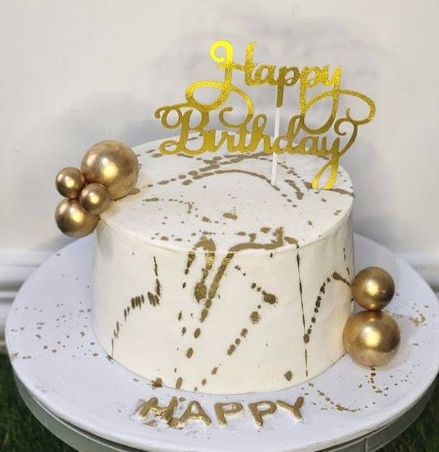 White marbled birthday cake with gold decorations and 'Happy Birthday' topper.