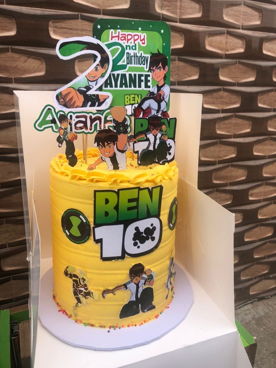 Yellow Ben 10 themed birthday cake with character decorations and personalized topper.