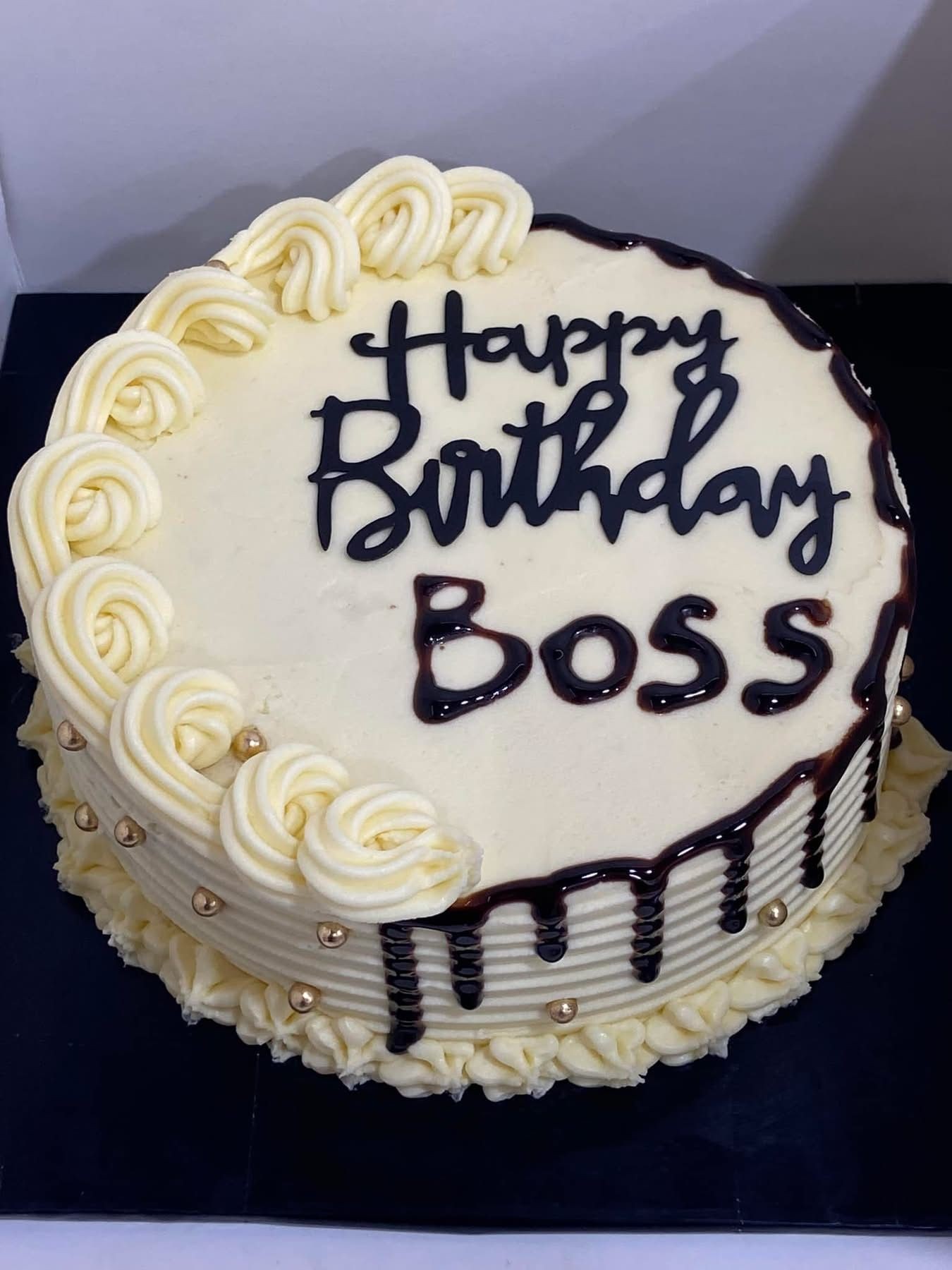 Round birthday cake with icing roses and chocolate drip, reading 'Happy Birthday Boss' on top.