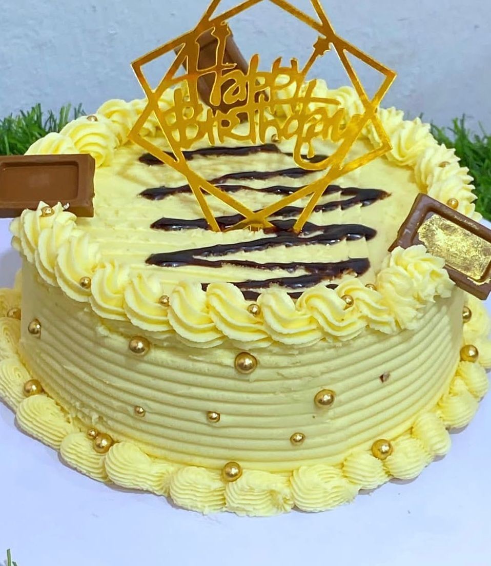 Decorative yellow birthday cake with gold topper, chocolate bars, and pearl accents.