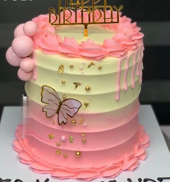 Pink ombre cake with butterfly decoration, pink spheres, and 'Happy Birthday' topper.