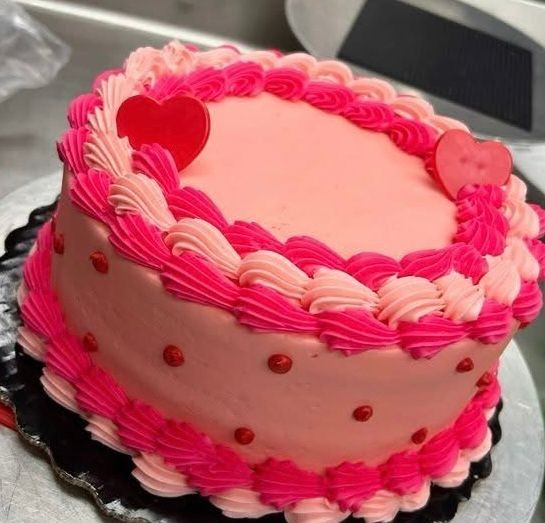 Pink frosted cake with heart decorations and piped border, on a black plate.