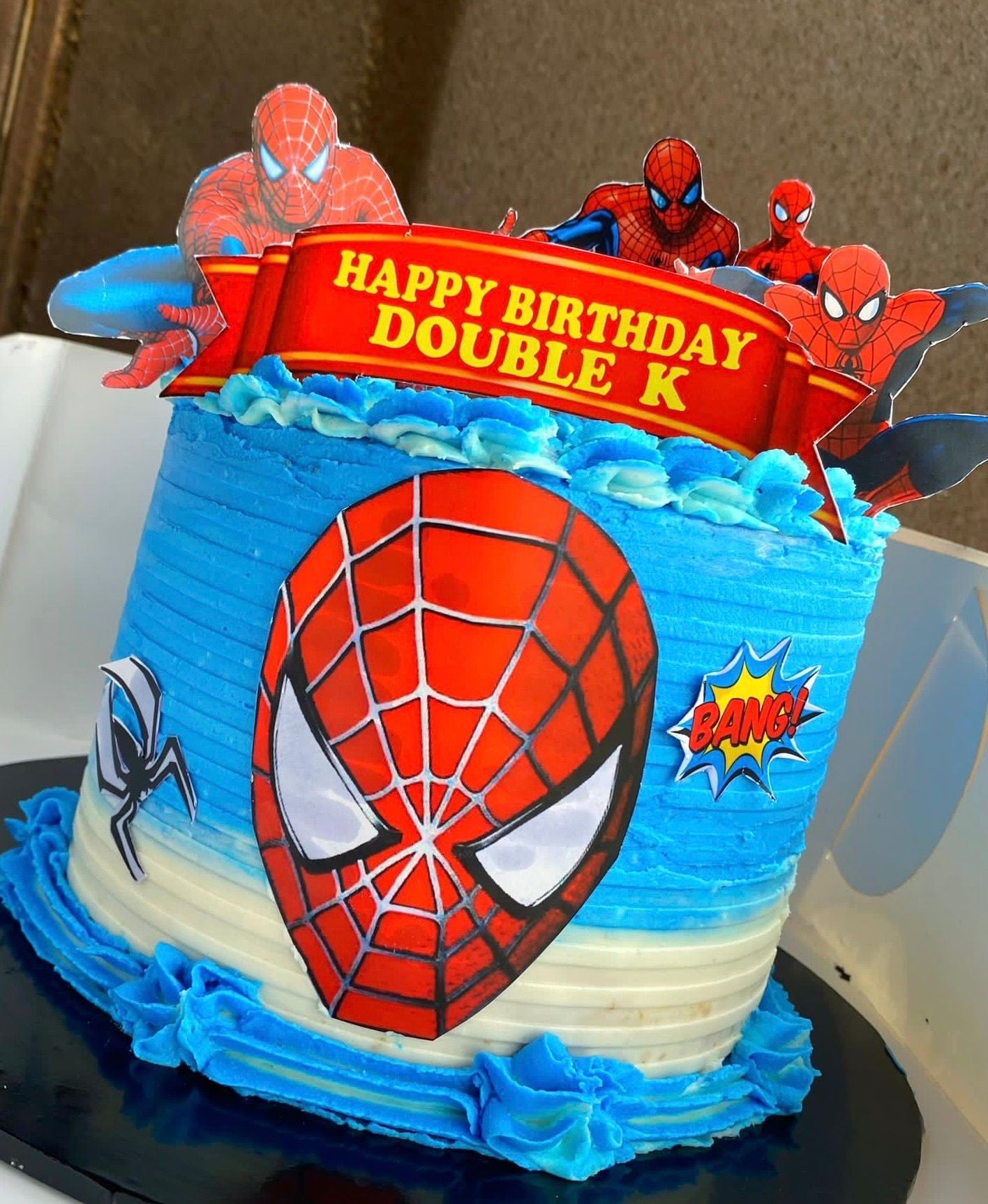 Spider-Man themed birthday cake with blue icing and decorations, featuring a message and comic-style accents.