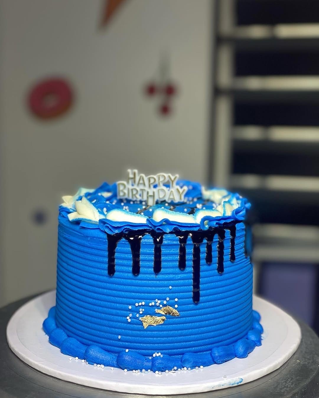 Blue birthday cake with white and dark blue frosting, topped with a 'Happy Birthday' sign.