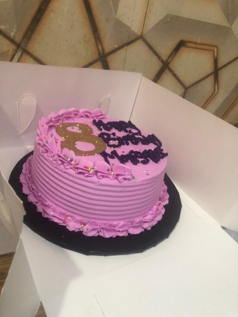 Purple birthday cake with ruffled icing and decorative words on top inside a white box.