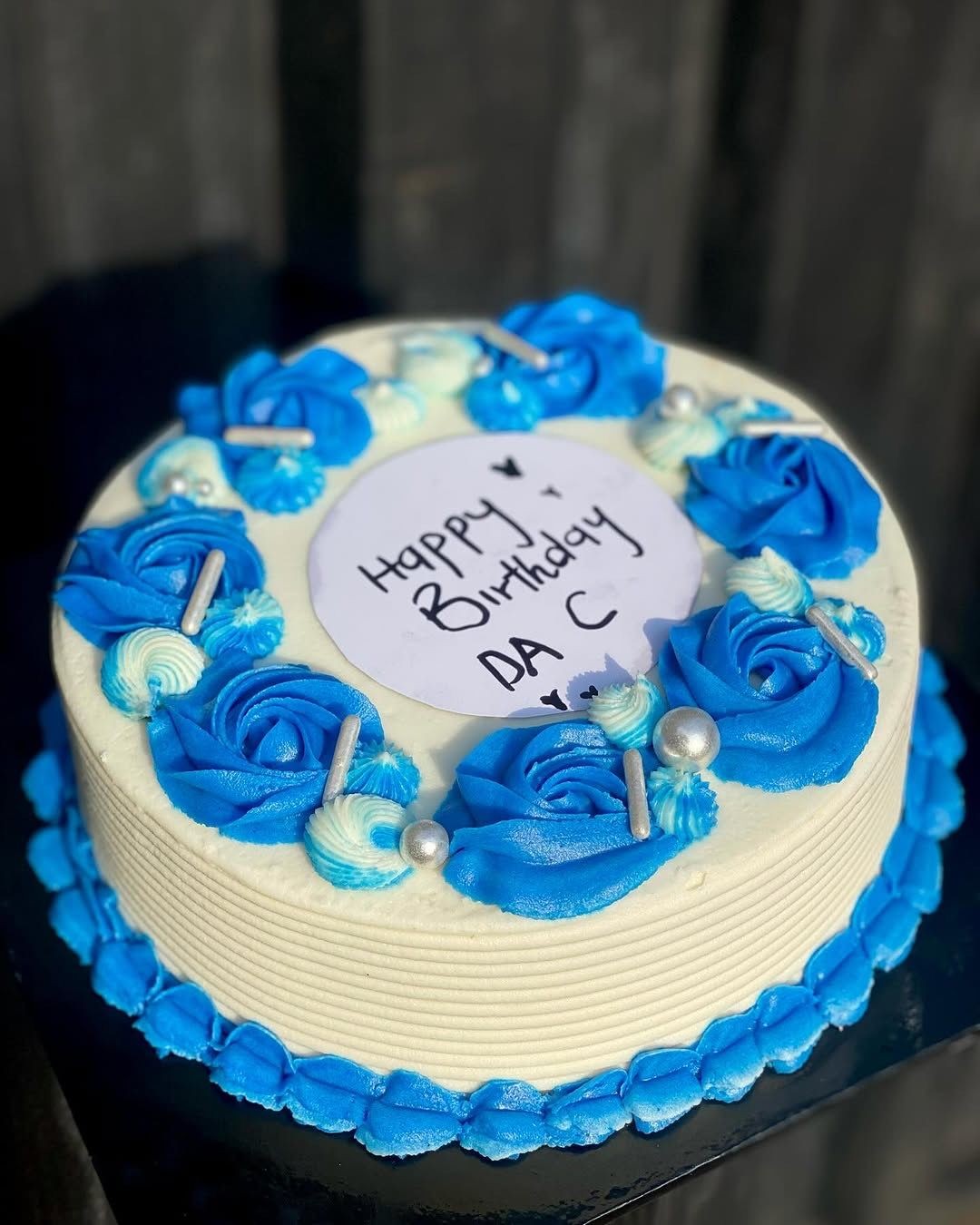 Vanilla birthday cake with blue and white roses and 'Happy Birthday DAC' message.