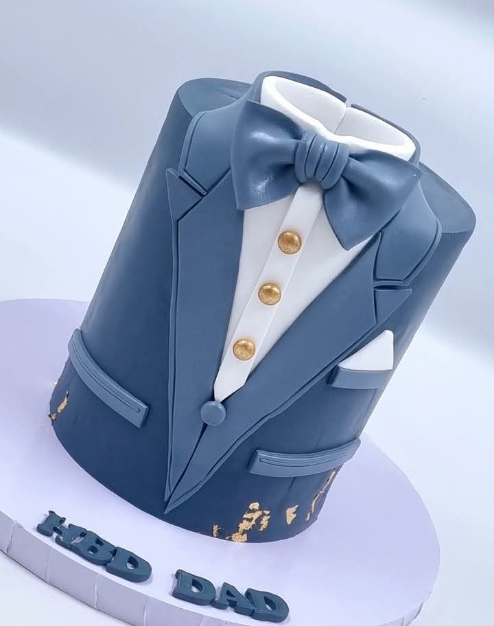 Cake designed to look like a blue suit with bow tie and golden buttons on a white base.