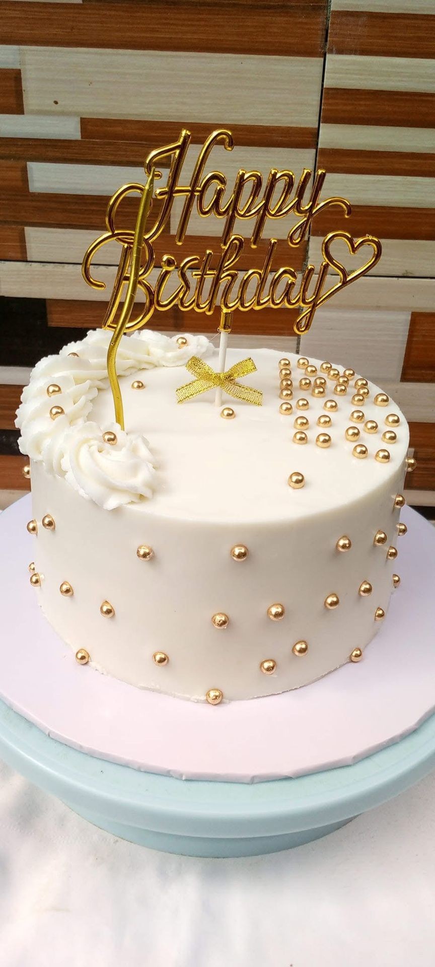 White birthday cake with gold decorations and 'Happy Birthday' topper.
