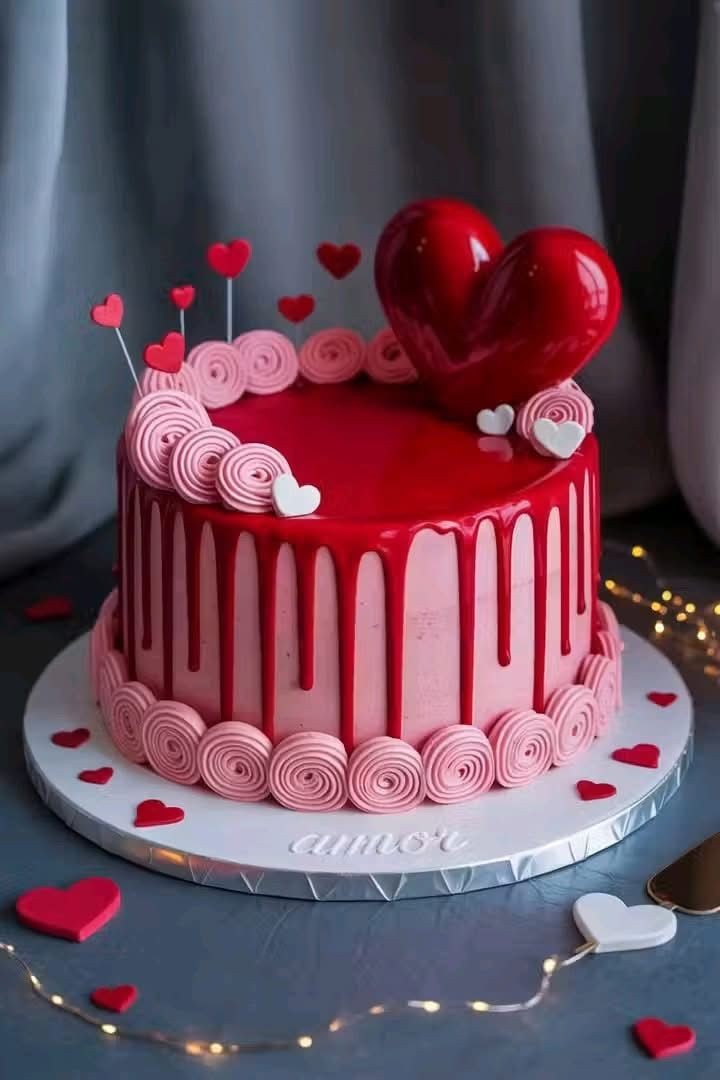 Pink and red heart-themed cake with swirl icing and a large heart topper on a decorated base.
