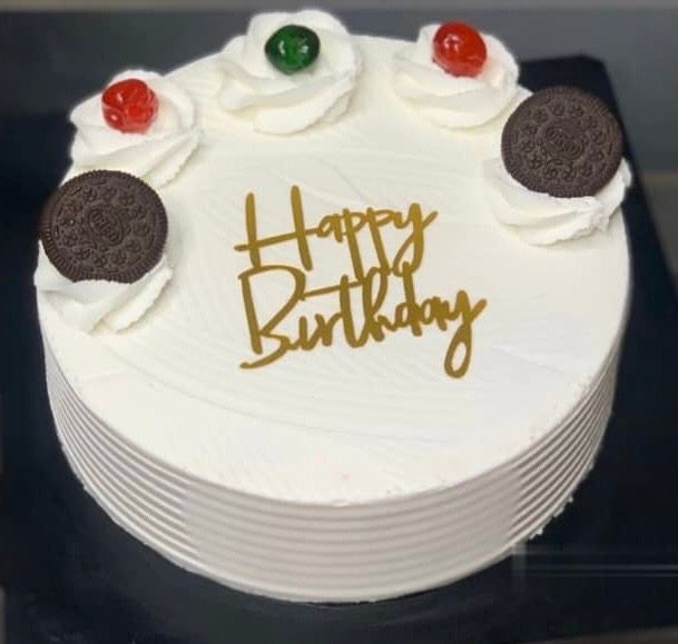 White birthday cake with 'Happy Birthday' message, topped with cherries, cream, and cookies.