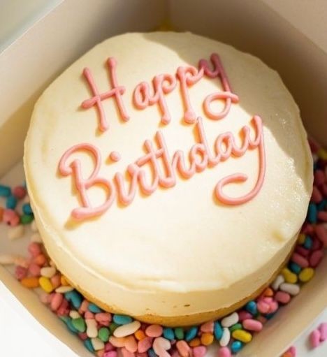 Birthday cake with 'Happy Birthday' written in pink icing on top, surrounded by colorful candies.