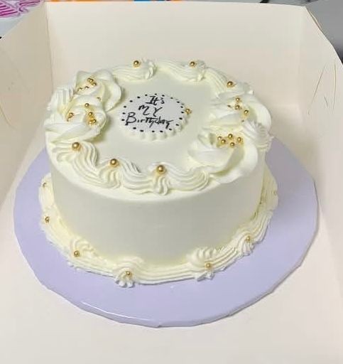 White birthday cake with decorative frosting and golden beads on a purple base.