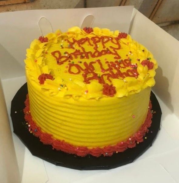 Yellow birthday cake with red icing flowers and sprinkles, featuring a message in red lettering.