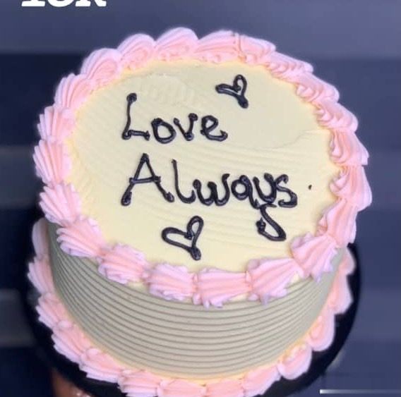 Yellow cake with pink frosting border, 'Love Always' written on top with heart decorations.