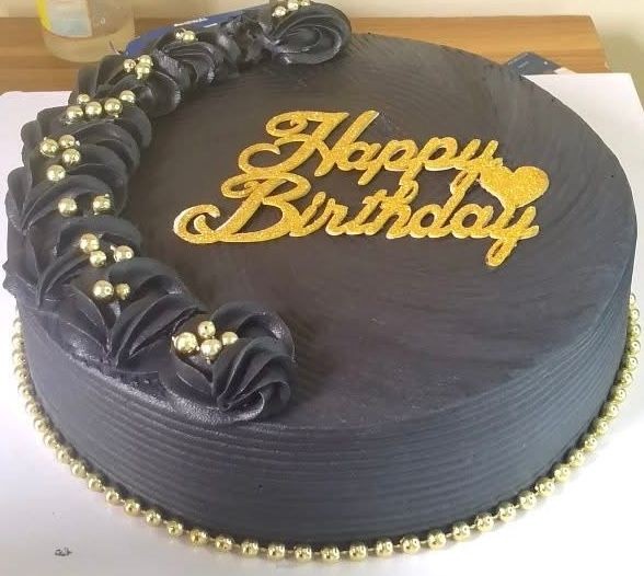 Black birthday cake with gold 'Happy Birthday' topper and decorations of black roses with gold beads.